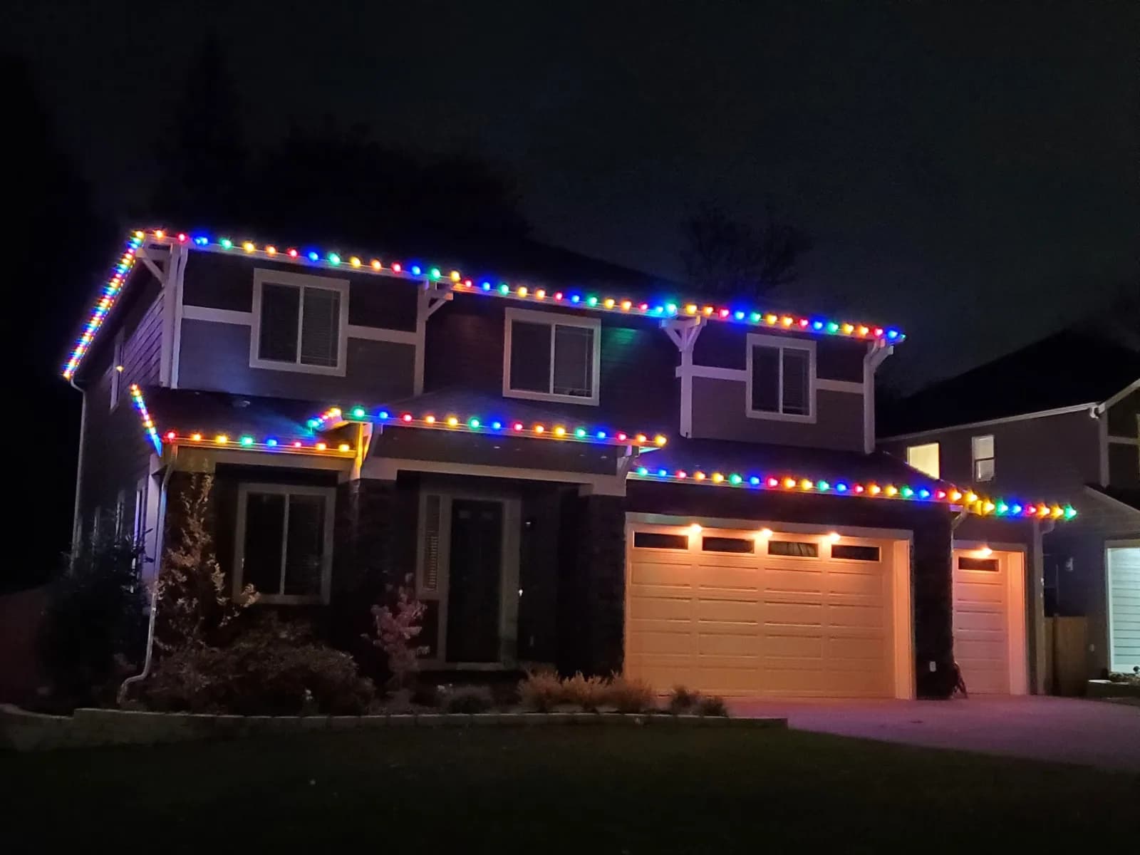 Two story home with multicolor holiday lights along the roofline and garage